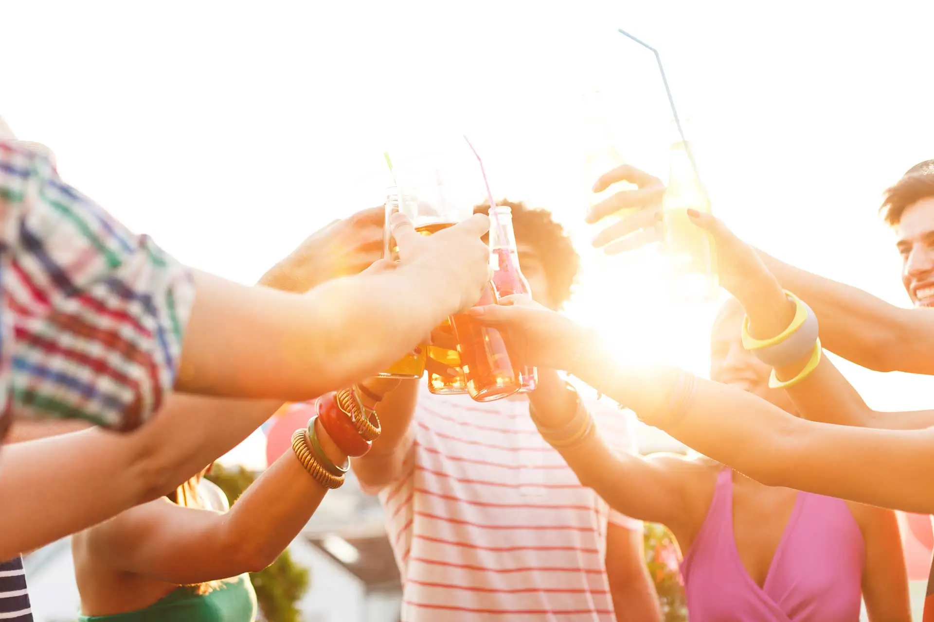 Group of friends clinking bottled drinks together in a celebratory toast outdoors at sunset.